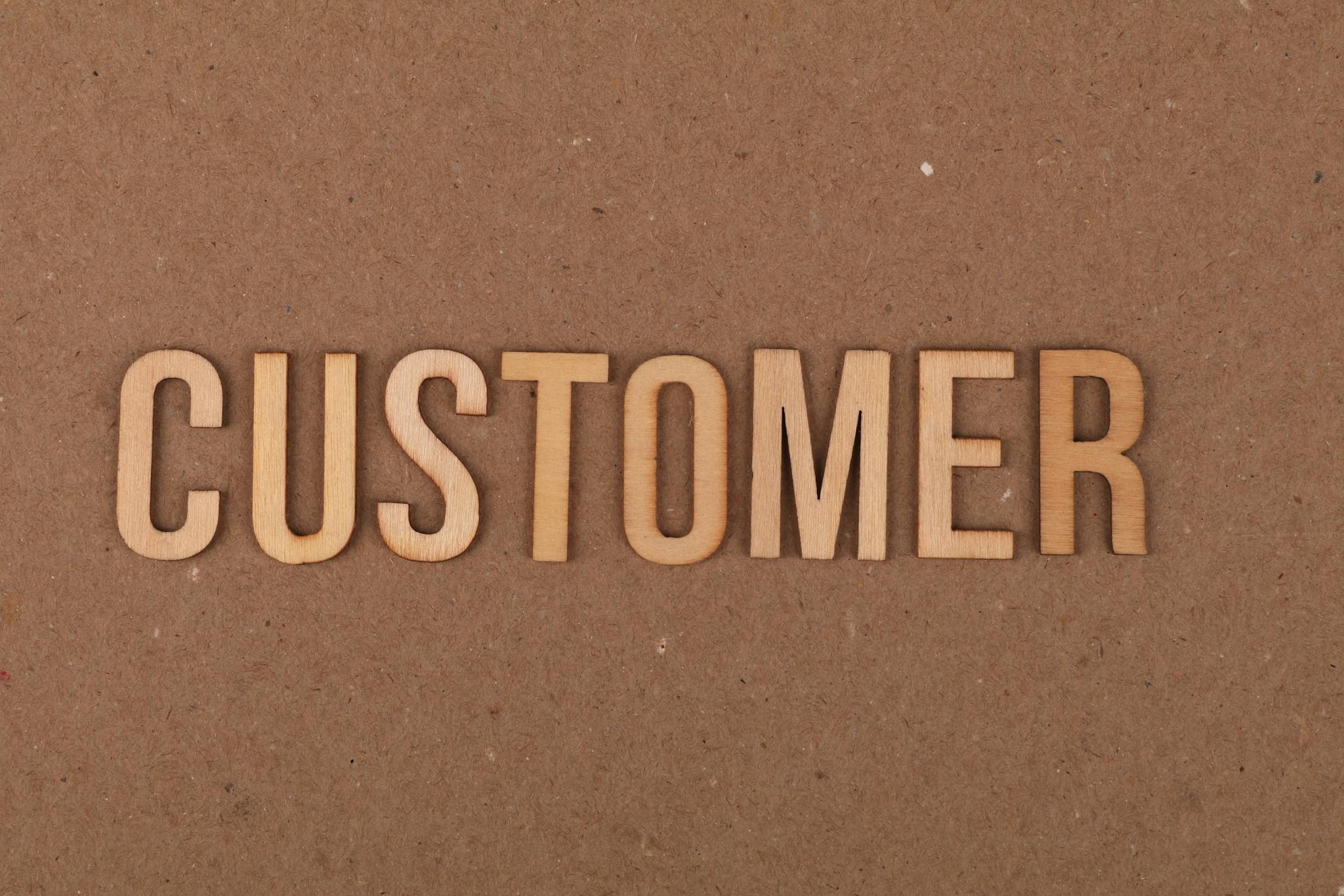 Wooden letters arranged to spell 'customer' on a plain cardboard surface for marketing concept.